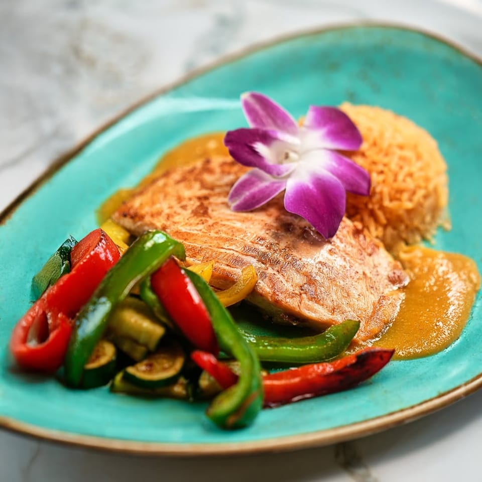 Mezcal's grilled salmon with colorful bell peppers, rice, and a purple orchid garnish on a blue plate.