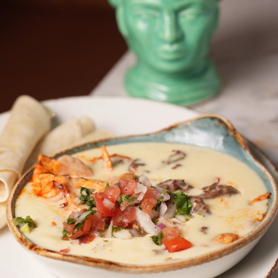 Mezcal's queso fundido with pico de gallo and tortillas, with a green statue in the background.