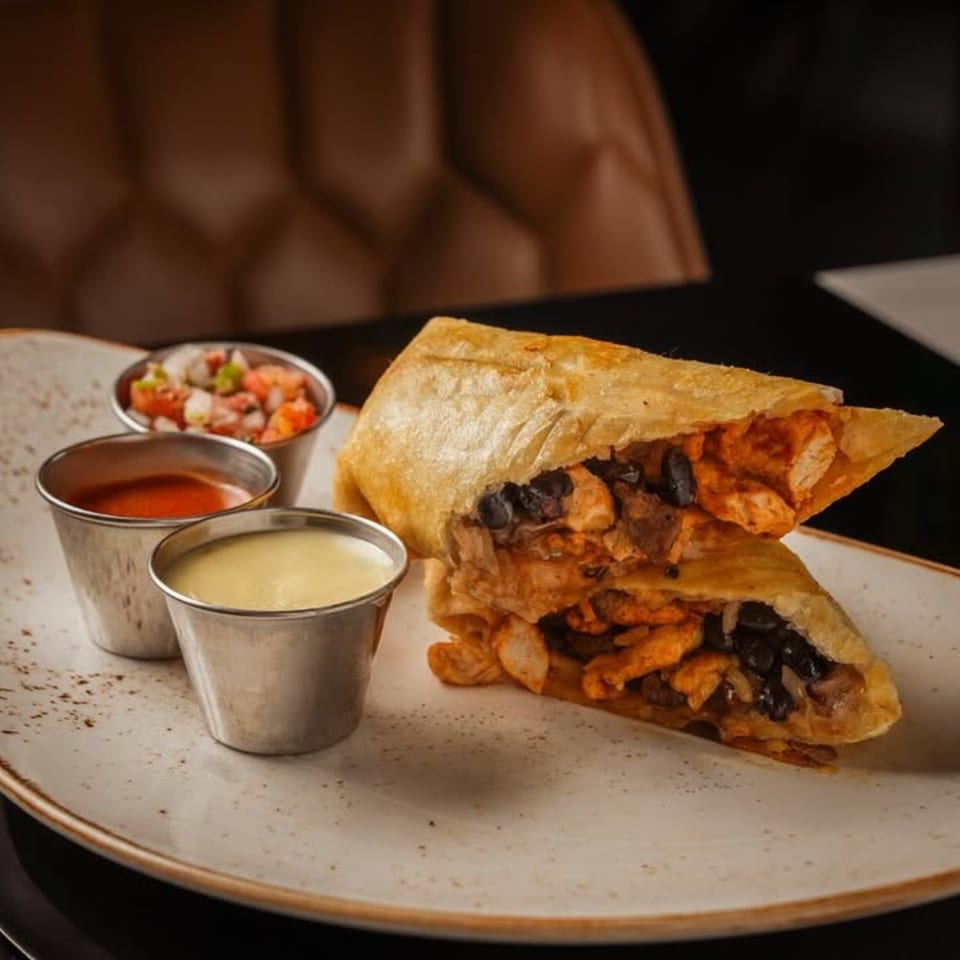 Crispy Mexican burrito, sliced in half, revealing chicken and black beans, served with three dipping sauces.
