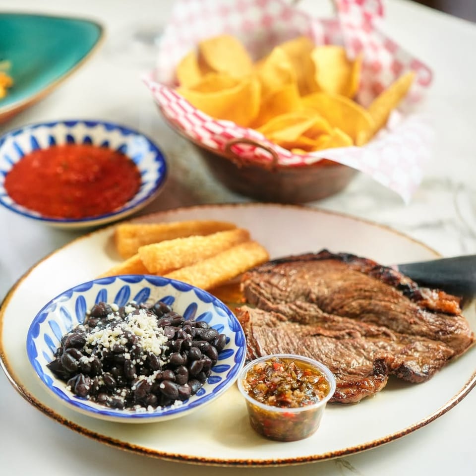 Mezcal's grilled steak with black beans, fried plantains, salsa, and a basket of tortilla chips.